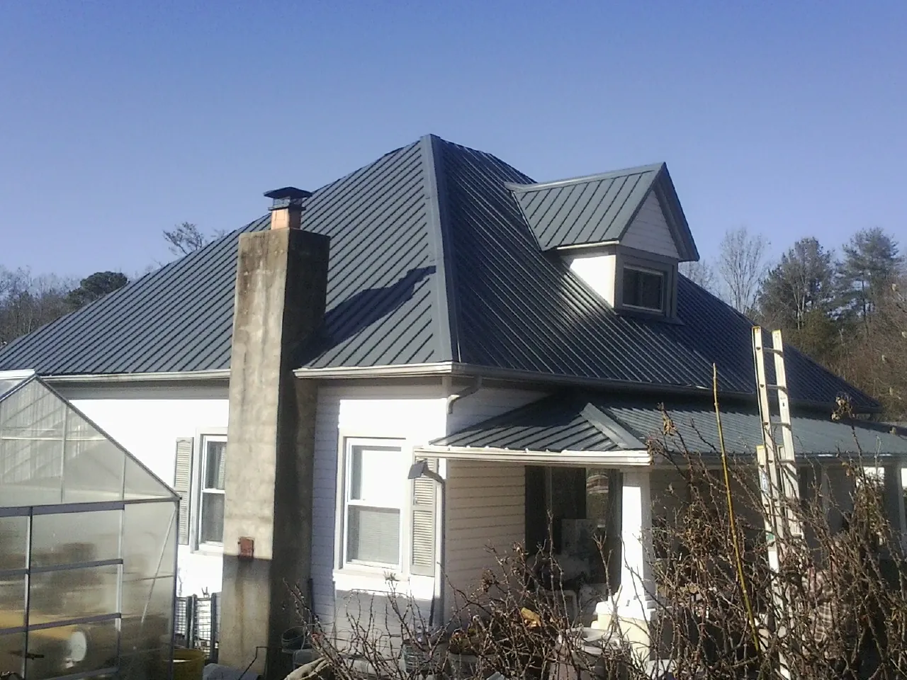 Dark blue standing seam metal roof on a white farmhouse with dormer — Slate & Tile Roof Repair by Roofing Brothers in Deatsville