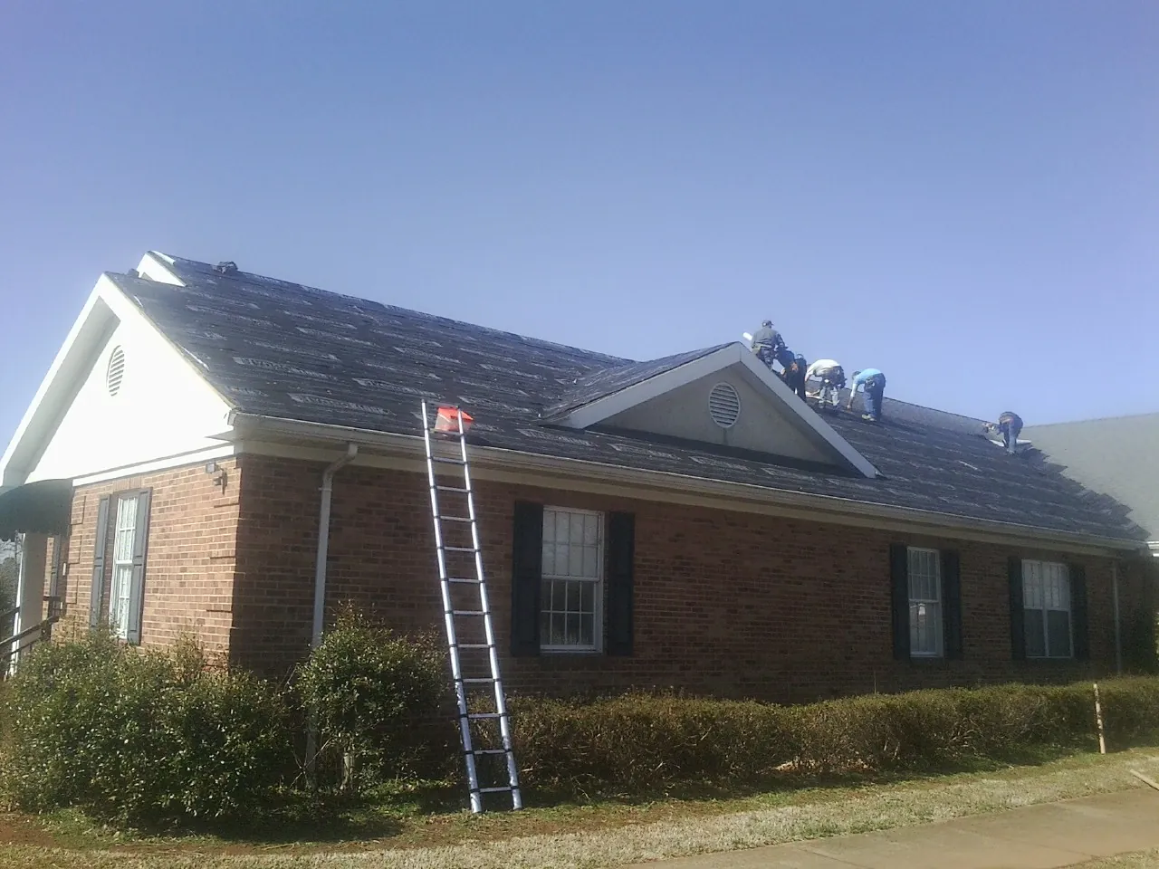 Crew tearing shingles off a brick ranch roof with a ladder set — Metal Roof Repair work by our crew in Deatsville