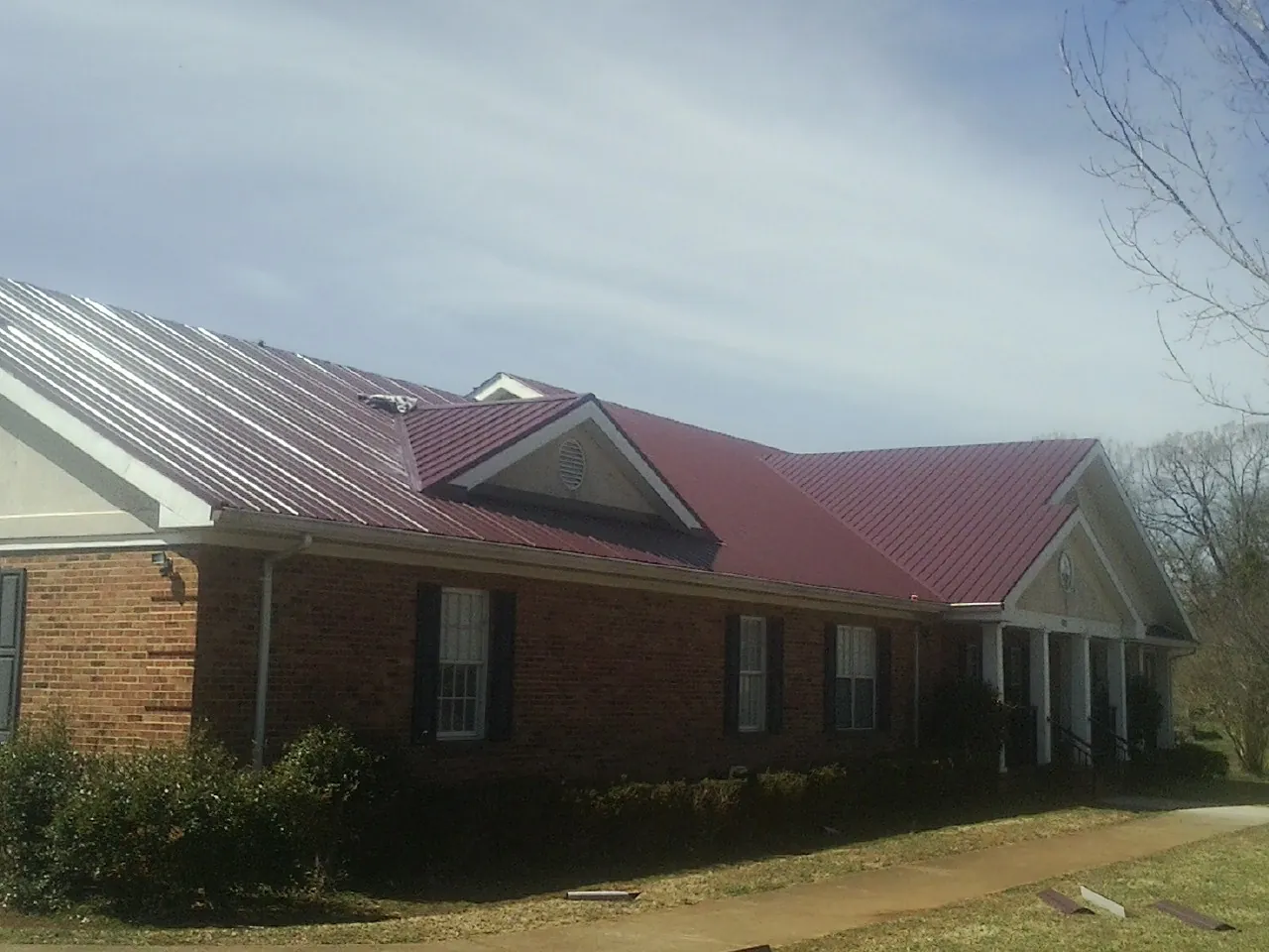 Red metal roof with gabled entries on a long brick building, from a Hail Damage Roof Repair job in Deatsville