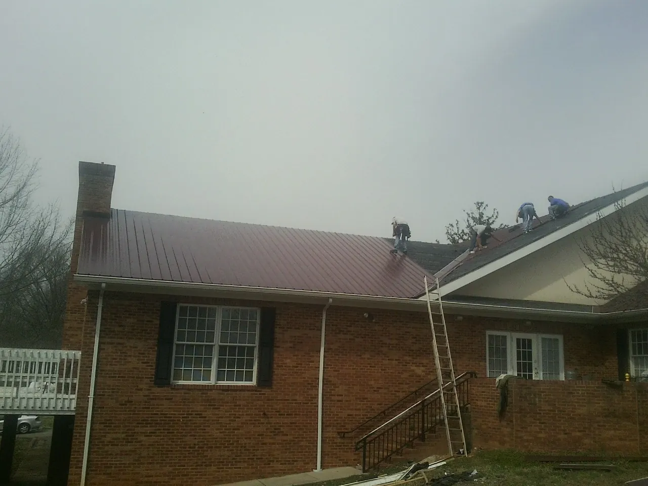 Crew setting red metal roofing panels on a brick home in Deatsville