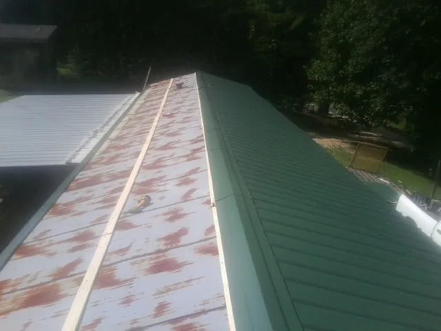 Old rusted panels beside newly installed green metal roofing — Wind Damage Roof Repair by Roofing Brothers in Deatsville