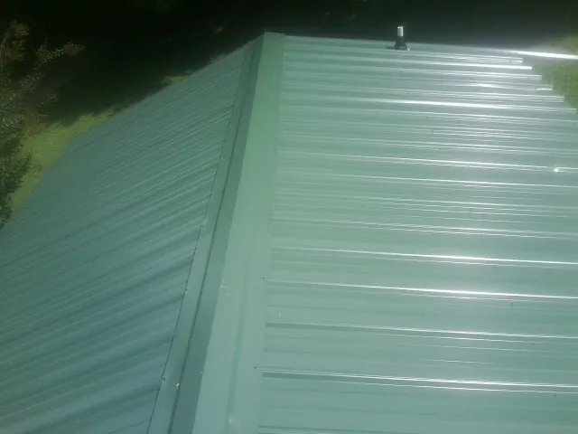 New green metal panels meeting at the ridge of a roof — Flat Roof Repair work by our crew in Deatsville
