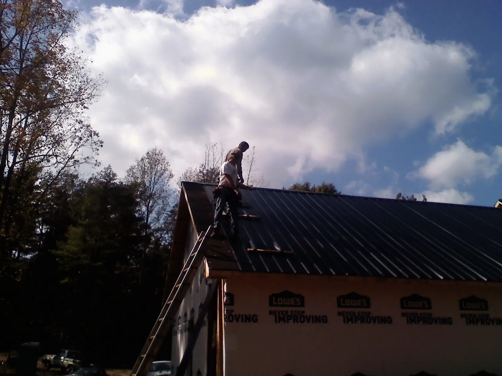 Roofer fastening dark metal panels high against a cloudy sky, from a Roof Inspection job in Deatsville