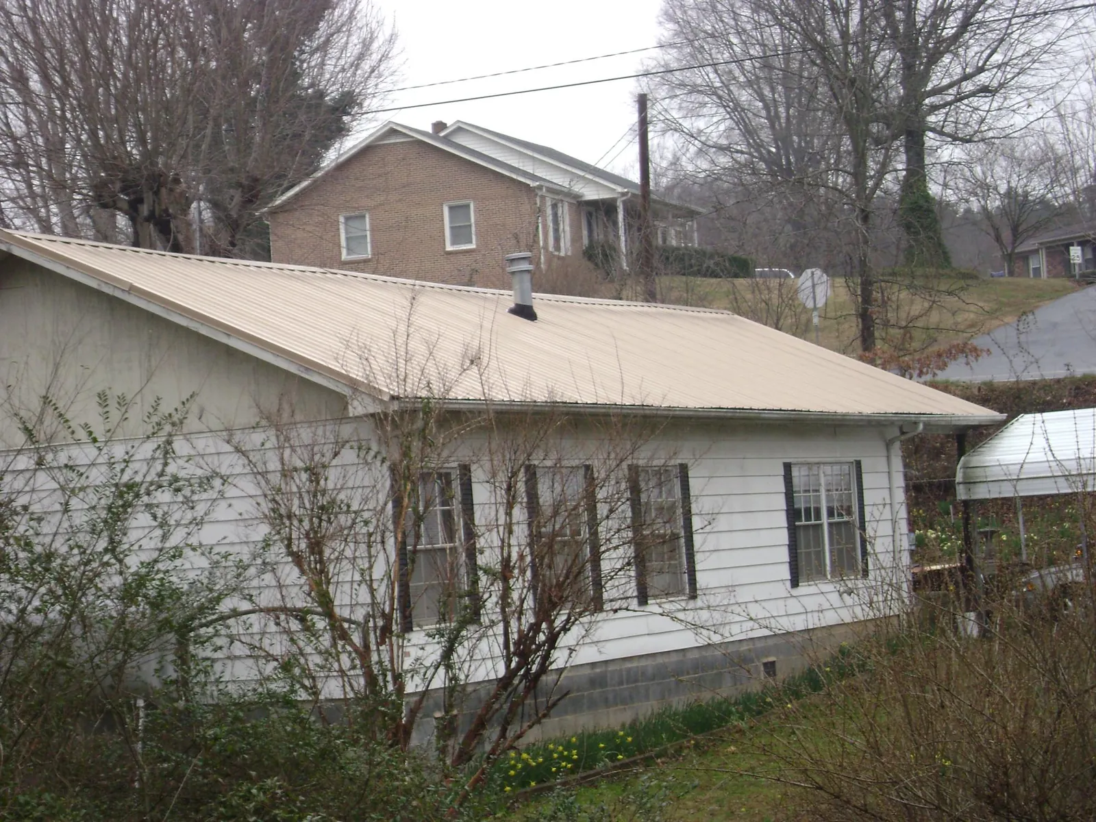Tan metal roof on a white sided house set into a hillside — Commercial Roofing by Roofing Brothers in Deatsville