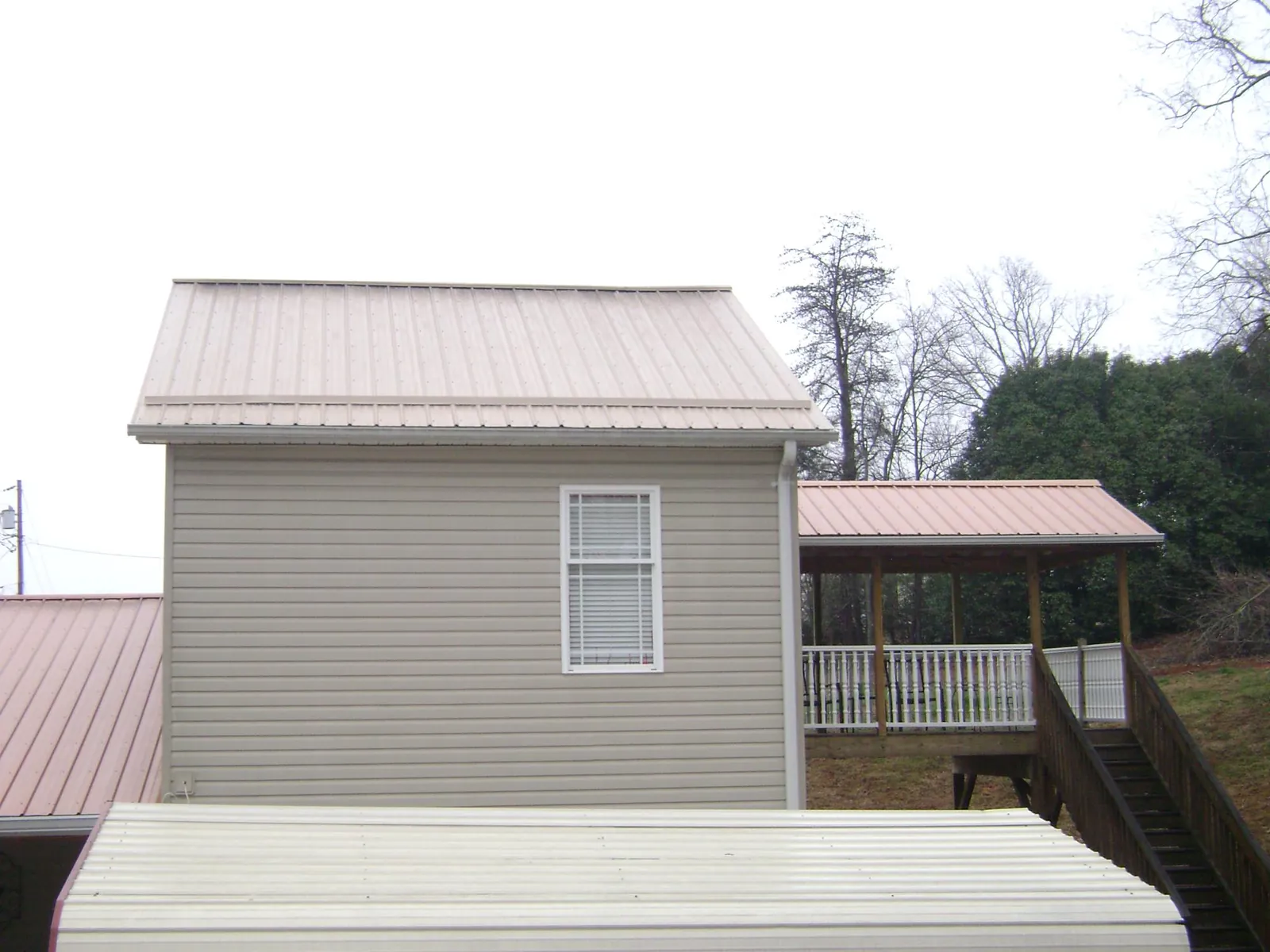 Tan metal roofs on a two story addition and attached porch, from a Roof Replacement job in Deatsville